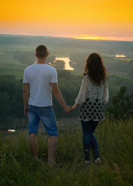 Romantic couple looking into the distance at sunset on outdoor, beautiful landscape and bright yellow sky, love tenderness concept, young adult people