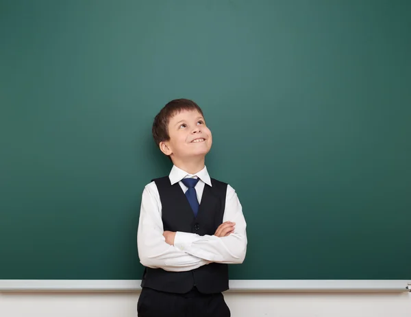 School student boy look up at the clean blackboard, grimacing and emotions, dressed in a black suit, education concept, studio photo