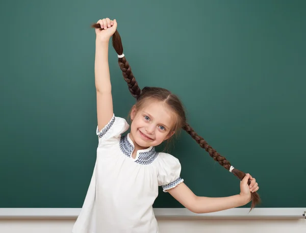 School student girl open arms at the clean blackboard, grimacing and emotions, dressed in a black suit, education concept, studio photo
