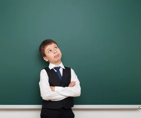 School student boy look up at the clean blackboard, grimacing and emotions, dressed in a black suit, education concept, studio photo