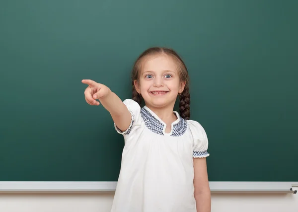 School student girl posing at the clean blackboard, grimacing and emotions, dressed in a black suit, education concept, studio photo