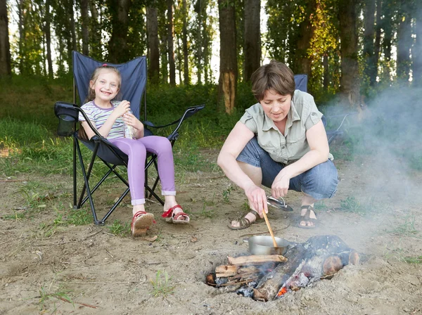 Woman cooking food, people camping in forest, family active in nature, child girl sit in travel seat, summer season