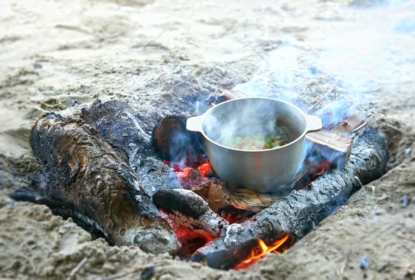 Cooking on fire at picnic, food prepared in kettle on wood, potatoes and tomatoes, healthy vegetarian food