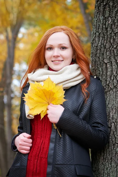 Redhead girl with leaf in city park, fall season