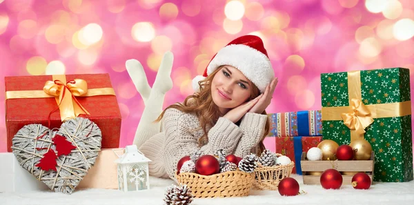 Beautiful young girl lie in santa hat with gift boxes - holiday concept