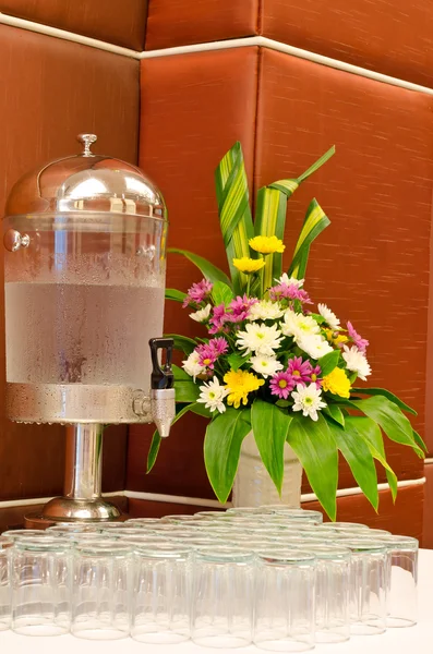 Water dispenser with glasses and flower vase on table at reception