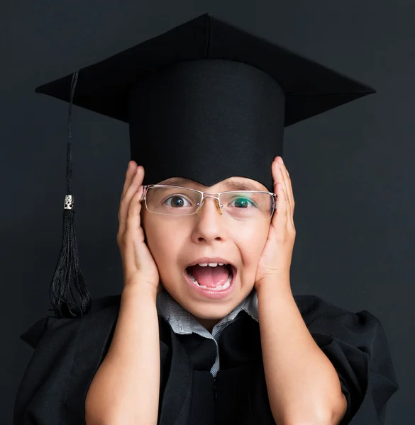 Portrait of shocked little girl wearing black graduation gown