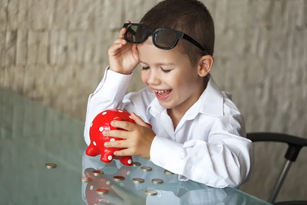 Happy little manager boy with coins and piggy bank