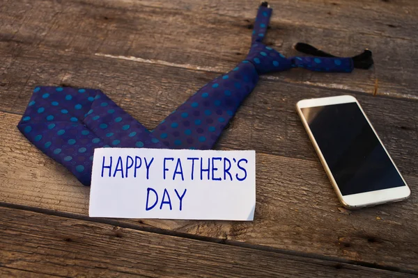 Happy Father\'s Day inscription with mobile phone and tie on wood