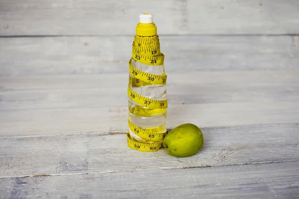 Yellow tape measure and a water bottle and apple on white wooden