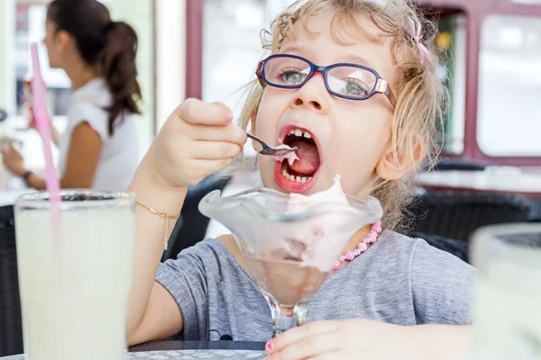 Little girl is eating ice cream at restaurant.