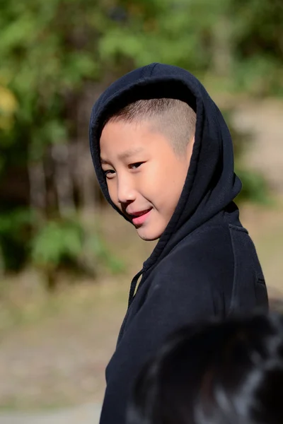 Asian boy in a black hooded sweat shirt with warm light outdoor.