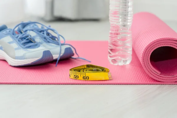 Sport shoes, yoga mat, bottle of water and centimeter on wooden