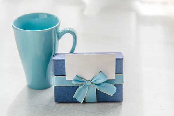 Blue gift box tea mug on gray wooden texture background with bla