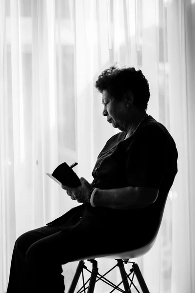 Black and white Asian senior woman  with holding pencil and note