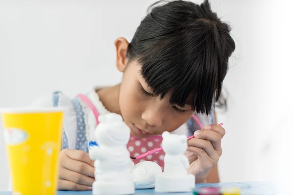 Asian child paints the colors of white plaster doll toys on the