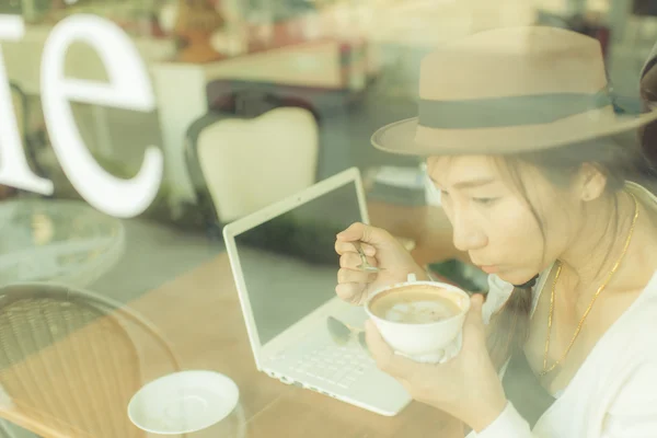 Asian woman drinking coffee and using computer in cafe.