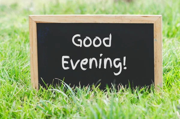 Good evening message on blackboard on green grass.