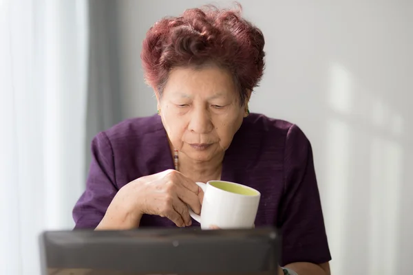 Asian senior woman learning notebook and drink a cup of tea at h