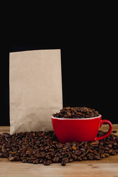 Coffee beans in red cup and brown paper bag on wooden table with