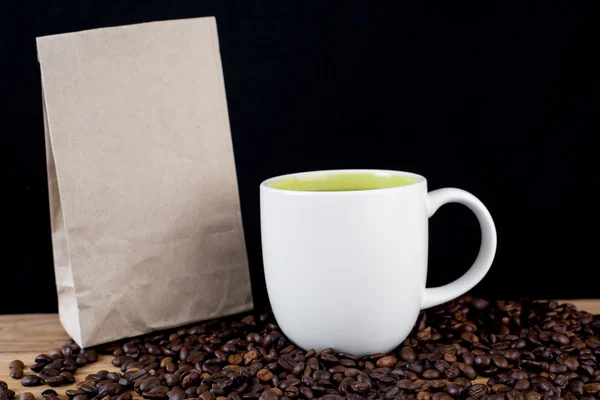 Coffee beans in white cup and brown paper bag on wooden table wi