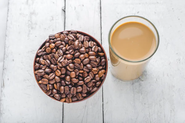 Coffee beans in bowl and a glass of coffee milk on wooden table.