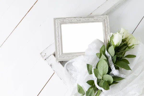 Empty silver picture frame with five white roses and lace ribbon