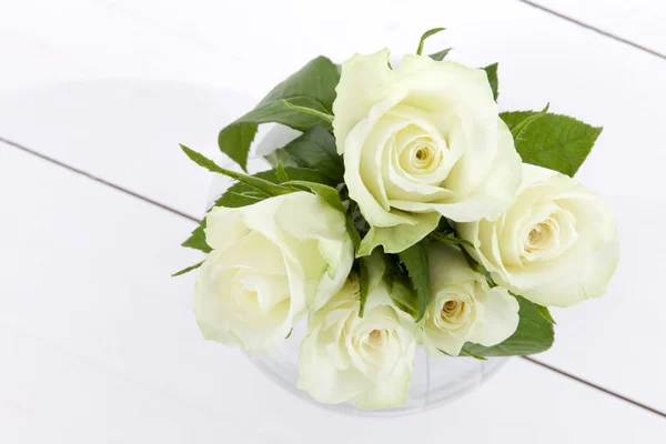 Five white roses and vase on white wooden floor