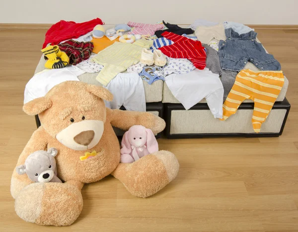 Bear toy on a bed with different colorful new born clothes.Colorful wardrobe of newborn,kids, babies full of all clothes, shoes,accessories and toys