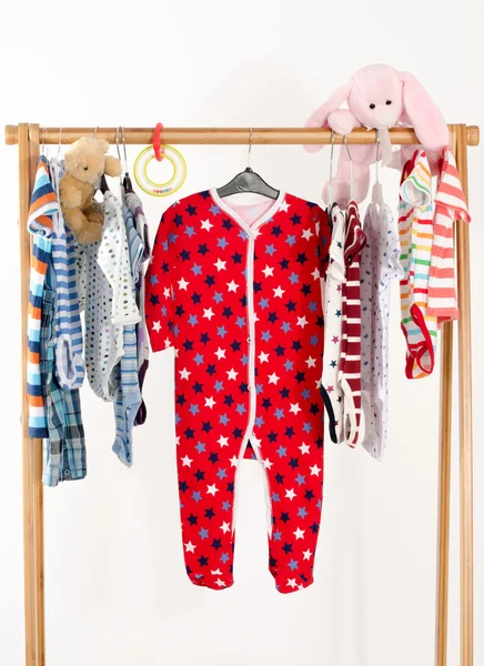 Dressing closet with clothes arranged on hangers.Colorful wardrobe of newborn,kids, toddlers, babies full of all clothes.Many t-shirts,pants, shirts,blouses, onesie hanging, bear and rabbit toy
