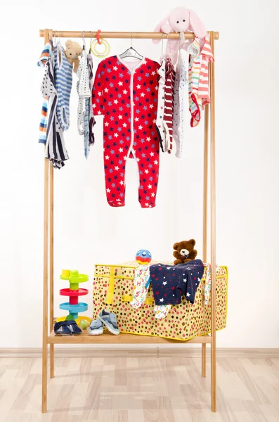Dressing closet with clothes arranged on hangers.Colorful wardrobe of newborn,kids, toddlers, babies full of all clothes.Many t-shirts,pants, shirts,blouses, onesie hanging, rabbit and bear toy