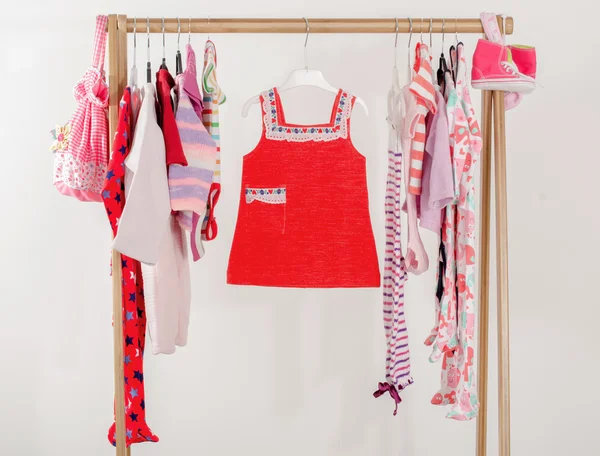 Dressing closet with clothes arranged on hangers.Red wardrobe of newborn,kids, toddlers, babies on a rack.Many t-shirts,pants, shirts,blouses, onesie hanging, little girl red dress