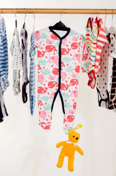 Dressing closet with clothes arranged on hangers.Colorful wardrobe of newborn,kids, toddlers, babies on a rack.Many t-shirts,pants, shirts,blouses, onesie on a rack, yellow bear toy hanging