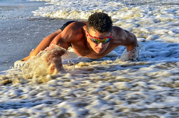 Strong bodybuilder with six pack.Fitness trainer with perfect abs, shoulders,biceps, triceps,chest, flexing his muscles on the beach, training in vacation, doing push ups in the sand