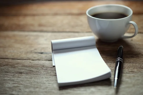 Open a blank white notebook, pen and cup of coffee on wood desk
