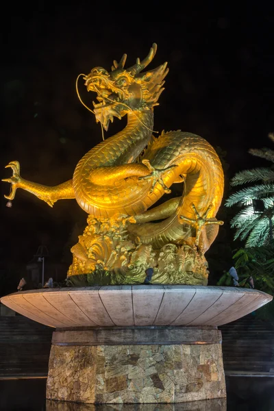 Phuket, Thailand - Jan 29, 2016: Beautiful gold colored dragon sculpture stands over a decorative fountain in night time at Phuket park.