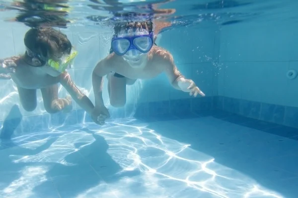 Two children diving in masks underwater in pool
