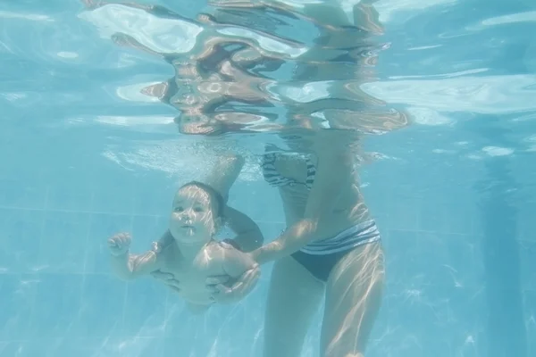 Baby child swimming under water with mother