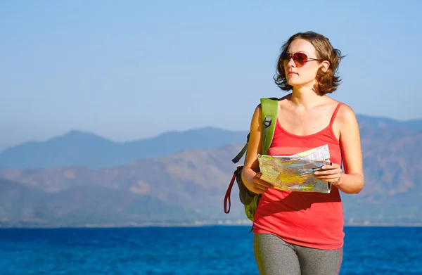 Young woman tourist walks on the seashore  reading the map.