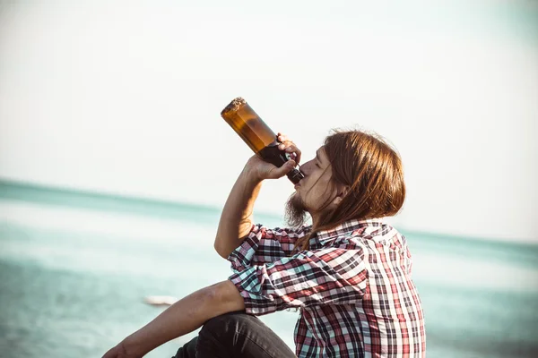 Man depressed with wine bottle sitting on beach outdoor