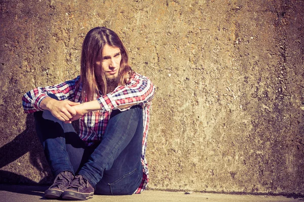 Man long haired sitting alone sad on grunge wall