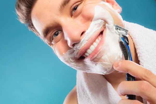 Happy man shaving using razor with cream foam.