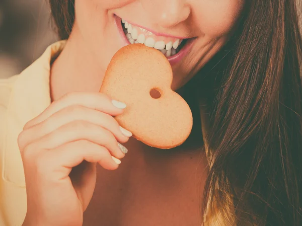 Girl eating biting gingerbread cookie.