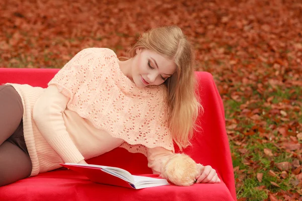 Woman relaxing in autumn fall park reading book.