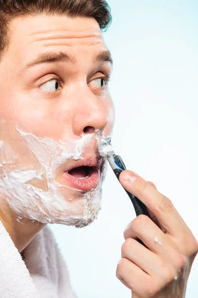 Young man shaving using razor with cream foam.