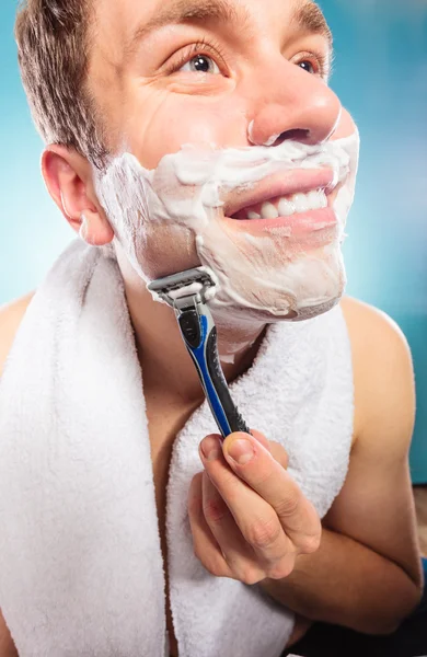 Happy man shaving using razor with cream foam.