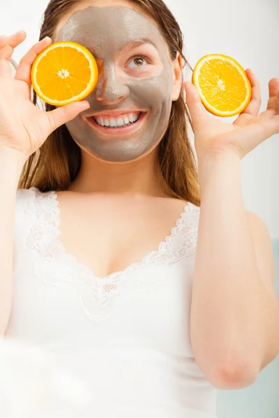 Woman with mud facial mask holds orange slice