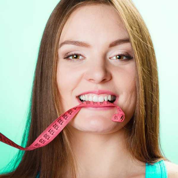 Attractive woman holding measuring tape between teeth.