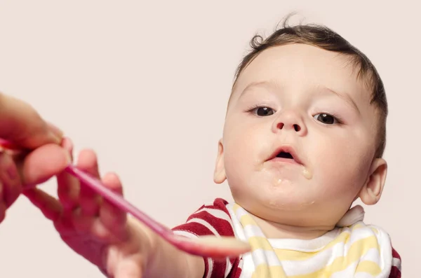 Mother hand feeding infant baby food. Child trying to grab the spoon.