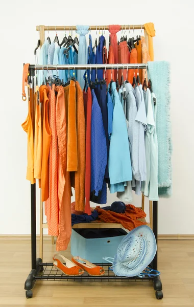 Wardrobe with complementary colors orange and blue clothes hanging on a rack nicely arranged.